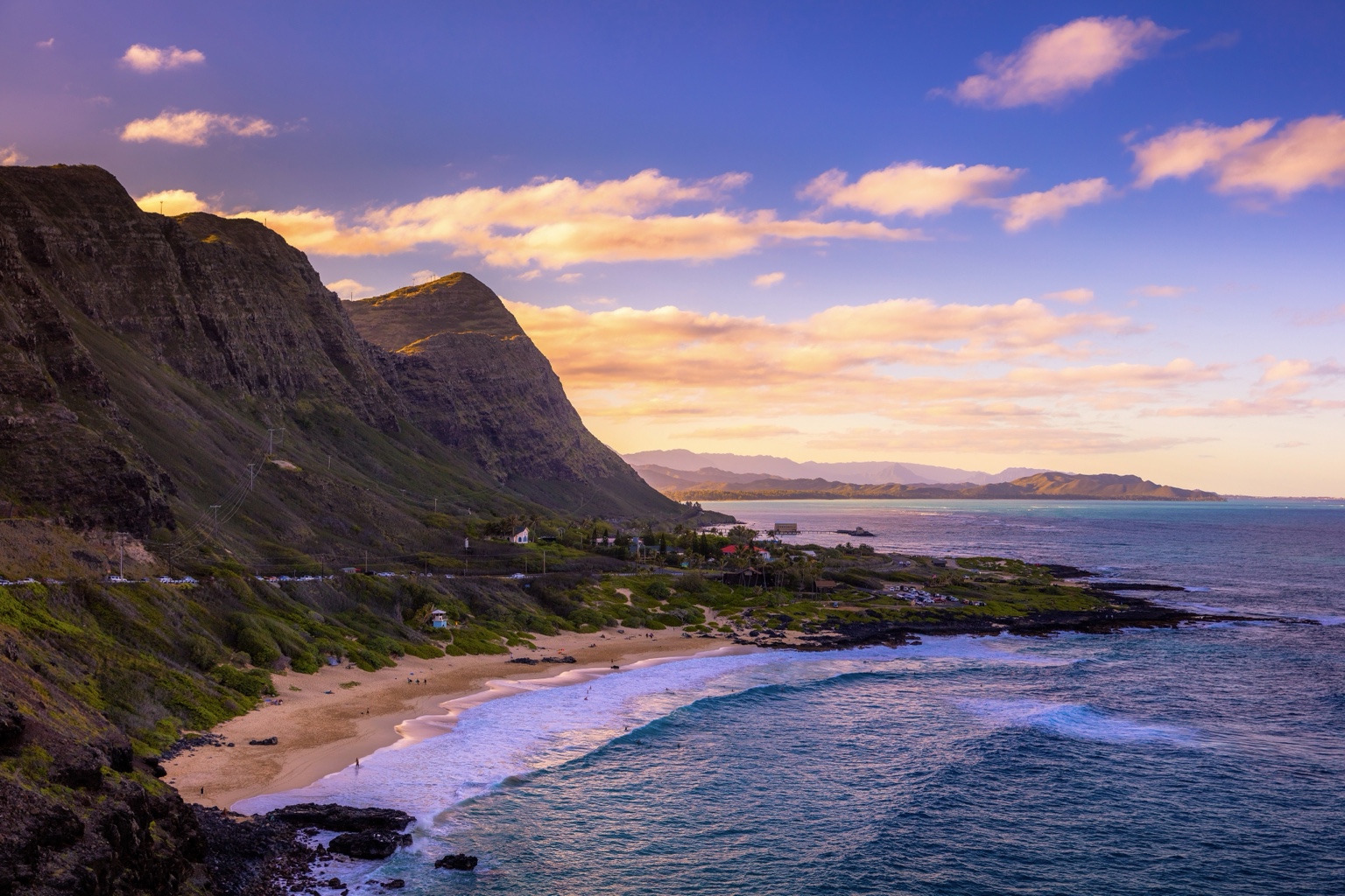 A sweeping beach beneath steep coastal cliffs, with soft evening light across the ocean.