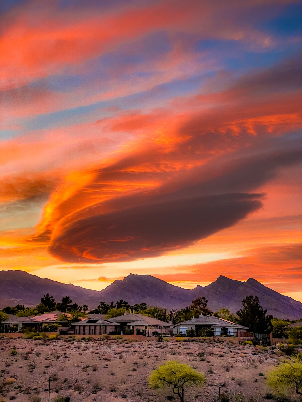 Brilliant orange sunset clouds over desert mountains and a quiet neighborhood.